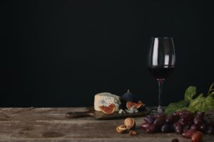 glass of red wine, cheese and fresh fruits on wooden table